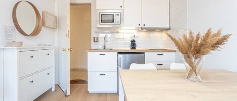 A modern kitchen with white cabinetry, a microwave, and a dining area with a wooden table and chairs.