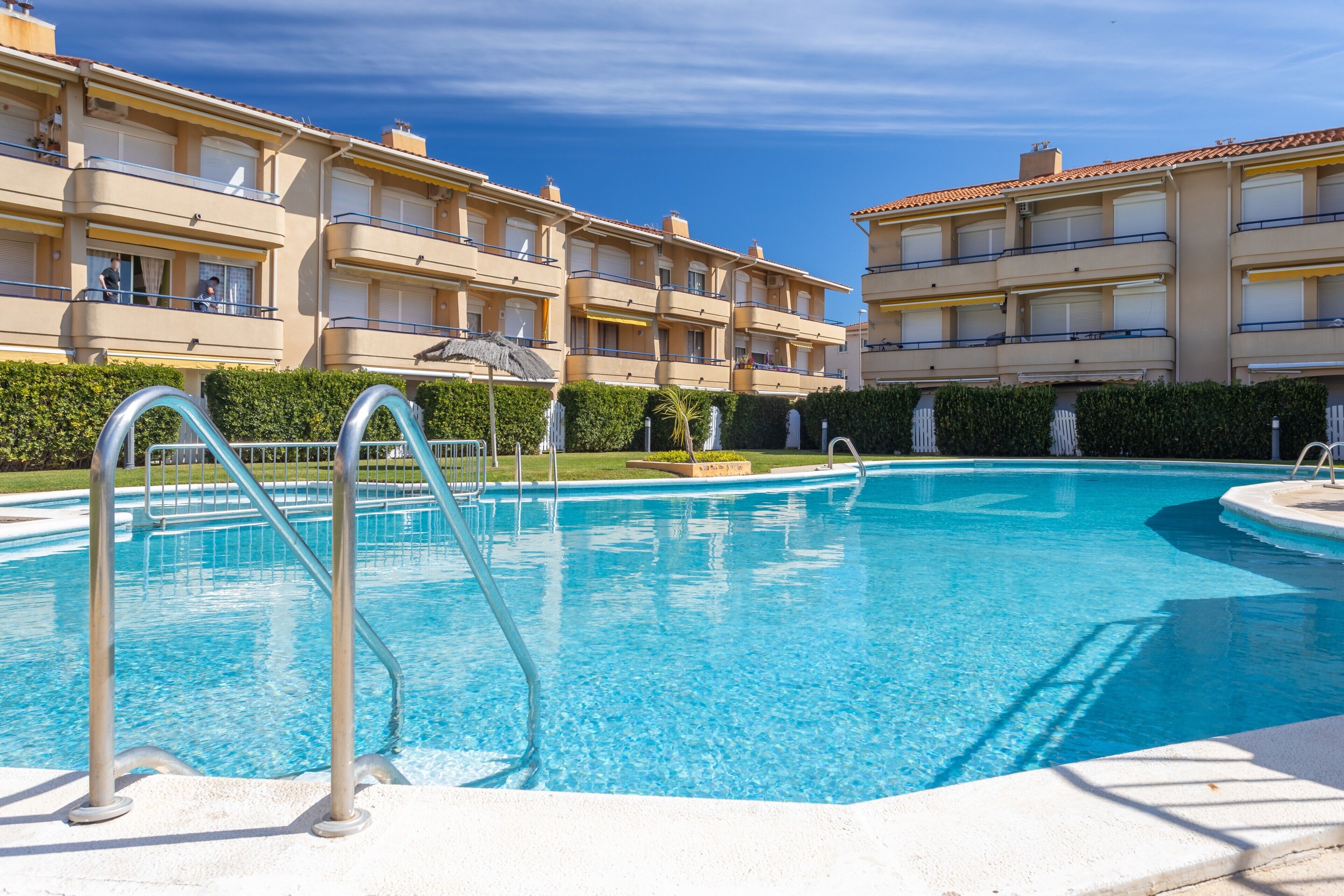 A swimming pool with a metal ladder, surrounded by a building with balconies and a clear blue sky.