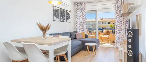 A modern living room with a dining table, chairs, a sofa, a TV, and a balcony with a view.
