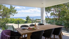Una mesa de madera con sillas de mimbre en un balcón con vistas a un paisaje marítimo y vegetación.