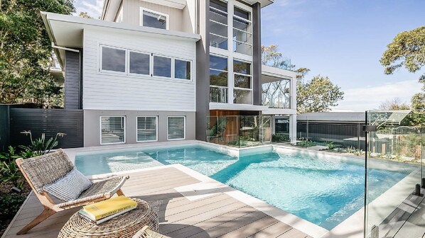 Una casa moderna de dos pisos con piscina, mobiliario exterior y vistas del entorno.