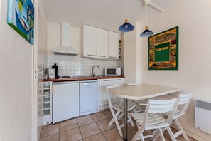 Een kleine keuken met witte kastjes, een magnetron, een vaatwasser, en een eethoek met een tafel en stoelen.