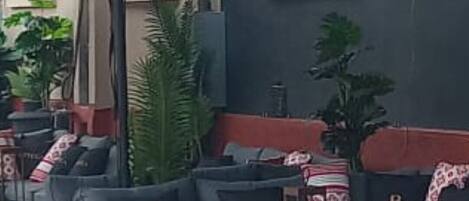An outdoor seating area with grey sofas, wooden tables, and potted plants.
