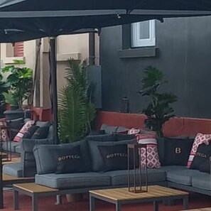An outdoor seating area with grey sofas, wooden tables, and potted plants.