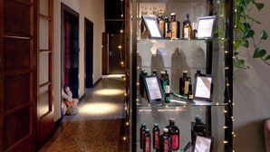 A hallway with a glass display case containing various bottles, a potted plant, and a sign. - Le Maginot Relais (Monticelli d'Ongina)
