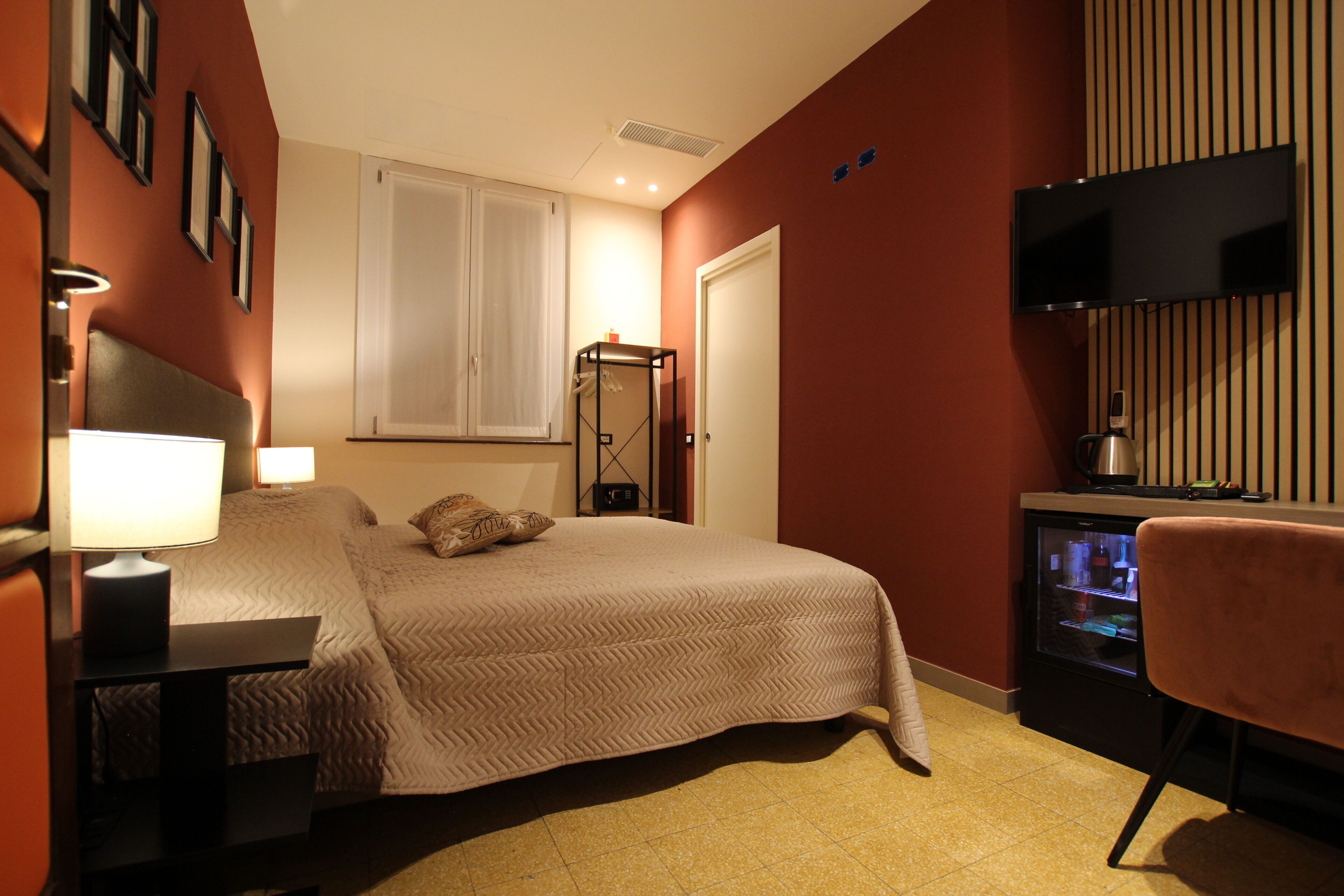 A bedroom with a bed, bedside table, lamp, TV, and a minibar.