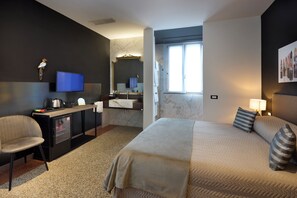 A hotel room with a bed, a desk with a television, a chair, a bathroom with a mirror, and a window.