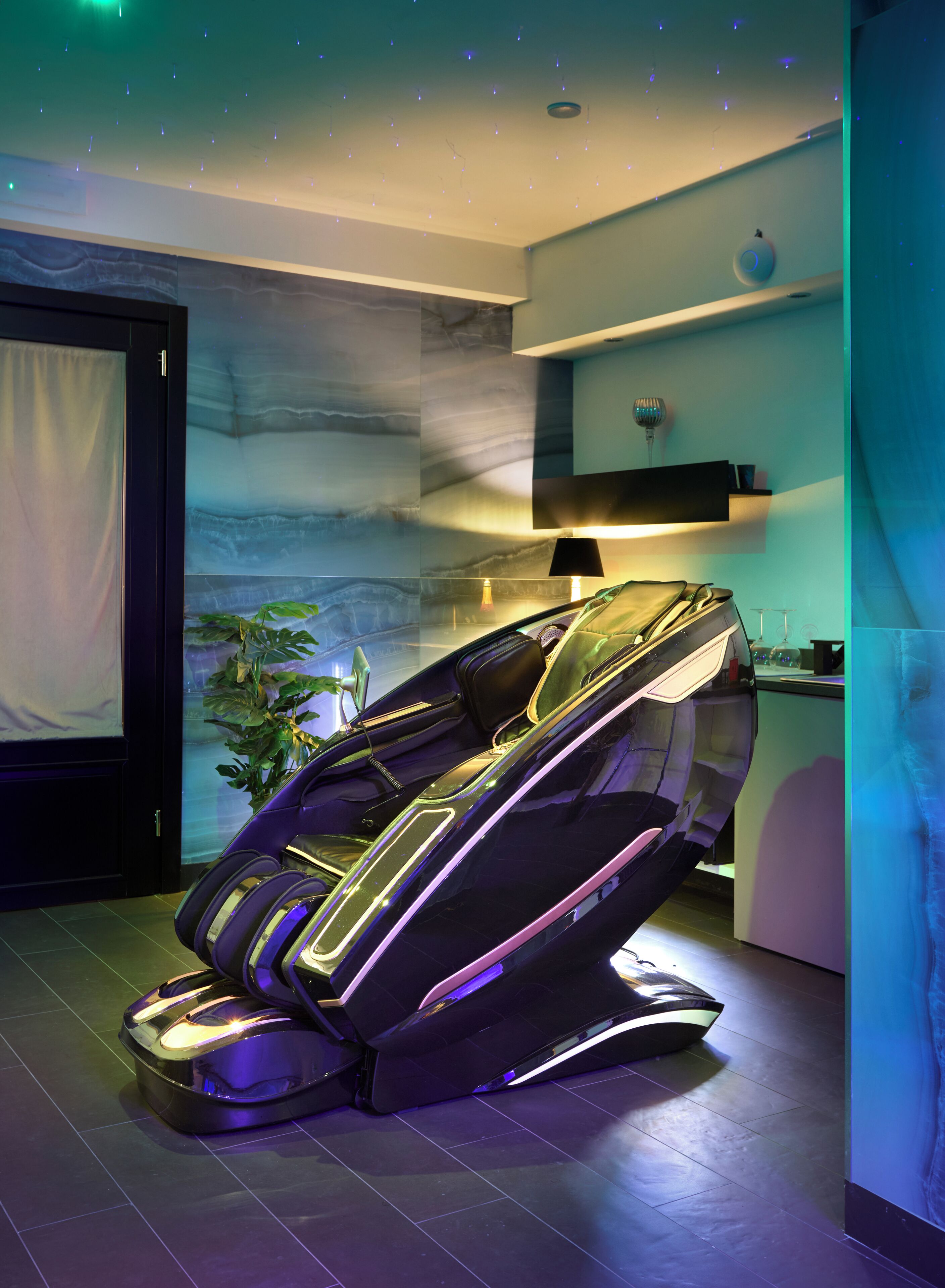 En massagefåtölj i ett modernt rum med en vägghängd hylla och en krukväxt.