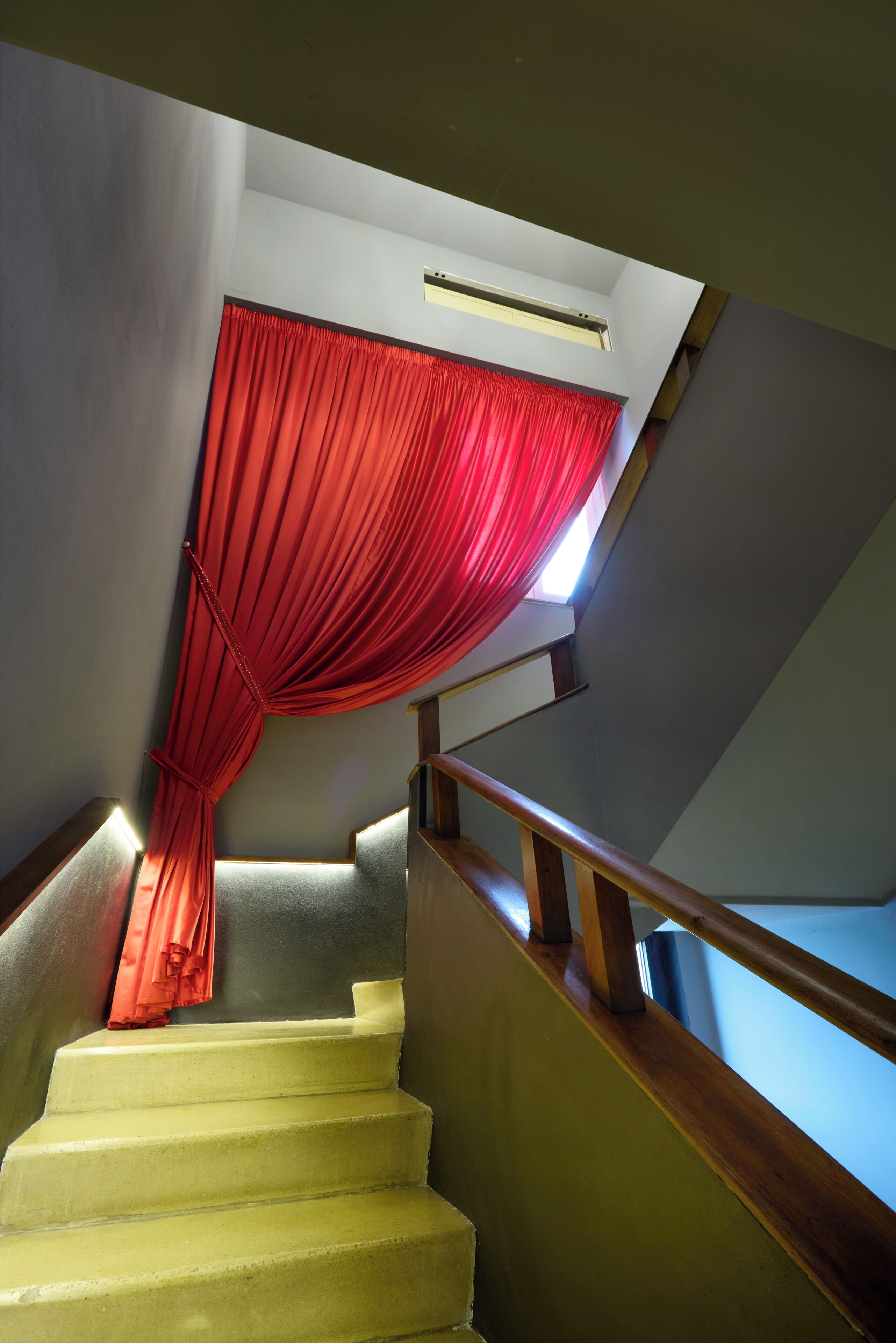 Uma escadaria com corrimão de madeira, cortina vermelha e luminária no teto.