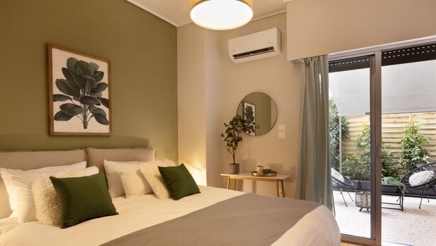 A bedroom with a large bed, a bedside table, a mirror, and a view of the outdoor patio. - Marina Zeas Apartment by the sea (Piraeus)