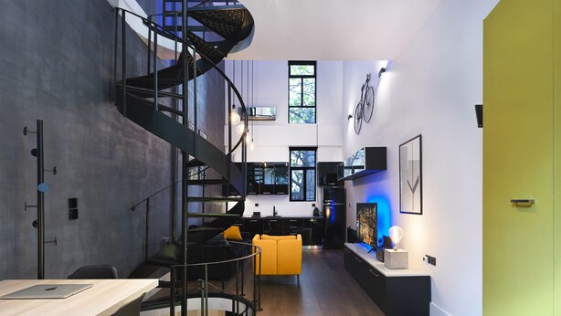 A modern kitchen with a spiral staircase, a dining area with a yellow chair, and a kitchen island with a light bulb. - 200mb Fibre Remote Workers' Dreamhouse (Athens)