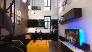 A modern kitchen with black cabinets, a yellow sofa, and a cityscape TV. - 200mb Fibre Remote Workers' Dreamhouse (Athens)