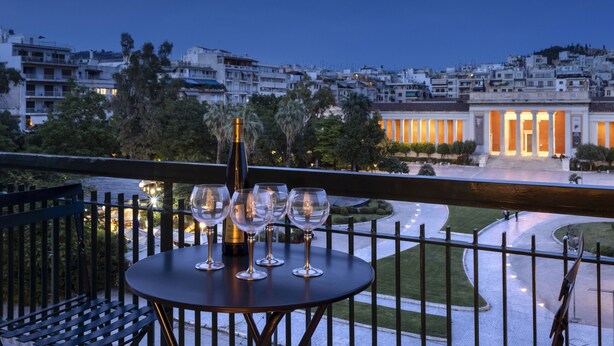 A balcony with a table set for four, overlooking a cityscape at dusk. - A Truly WOW Experience for Every Guest (Athens)