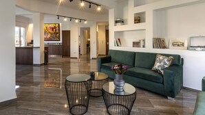 A spacious living area with a green sofa, two round tables, and a large abstract painting on the wall. - A Truly WOW Experience for Every Guest (Athens)