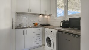 Une cuisine moderne avec des armoires blanches, un four encastré, un lave-linge et une fenêtre donnant sur le ciel.
