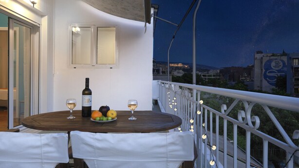 Un balcon avec une table dressée pour deux personnes, agrémenté d’une bouteille de vin, de verres et de fruits.