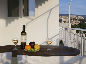 A table with a bottle of wine, two glasses, and a plate of fruit on a balcony overlooking a cityscape. - Acropolis View top Floor Apartment (Athens)