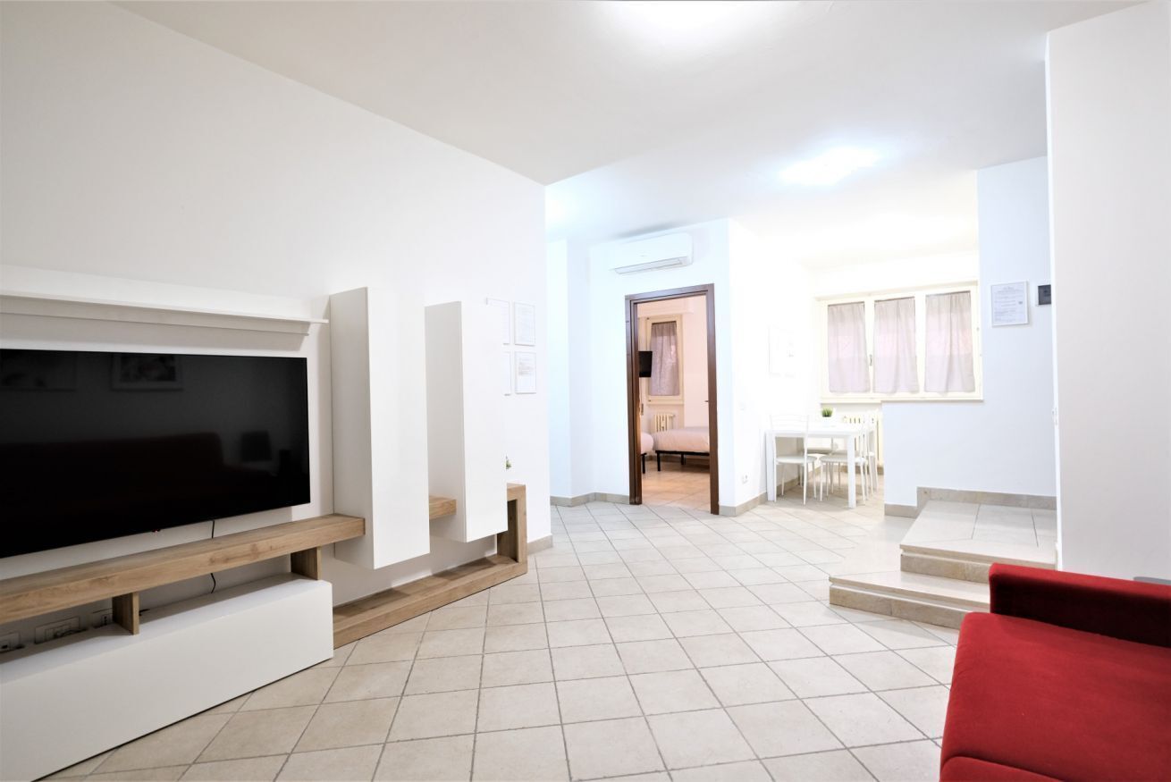 A spacious living area with a flat-screen TV on a wooden stand, a red sofa, and a dining area with a table and chairs.