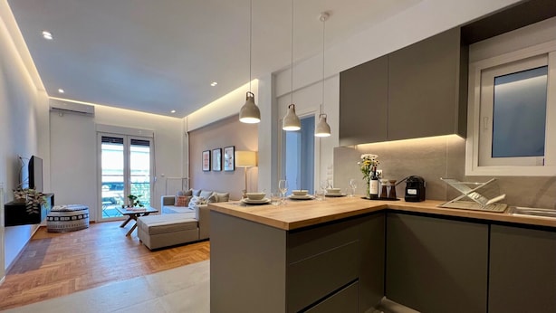 A modern kitchen with a central island, pendant lighting, and a view to the living area. - Nea Smirni Square Chic Apartment (Nea Smirni)