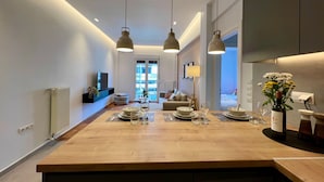 A modern kitchen with a central island, pendant lighting, and a view to a living area. - Nea Smirni Square Chic Apartment (Nea Smirni)