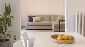 En moderne stue med en hvid sofa, et spisebord med stole og en potteplante.
