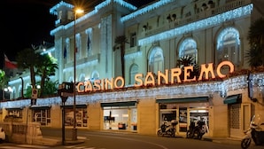 Un bâtiment doté d’une enseigne lumineuse indiquant « CASINO SANREMO » et d’une grande entrée en arc de cercle.