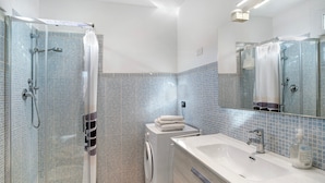 Une salle de bain moderne avec une douche à parois de verre, un lavabo blanc et un mur recouvert de carreaux.