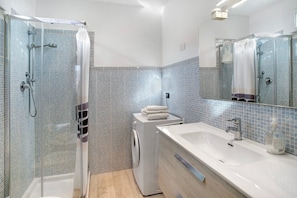 Een moderne badkamer met een douchecabine van glas, een witte wastafel en een betegelde spatwand.