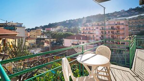Un balcon avec une table et des chaises, donnant sur une colline parsemée de bâtiments.