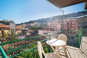 Een balkon met een tafel en stoelen, met uitzicht op een heuvel met gebouwen.