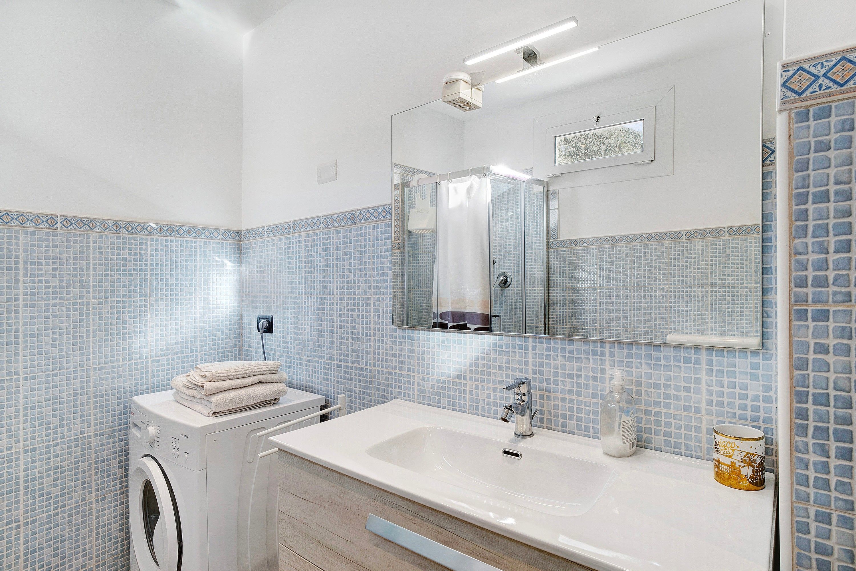 A bathroom with a washing machine, a sink, and a shower.