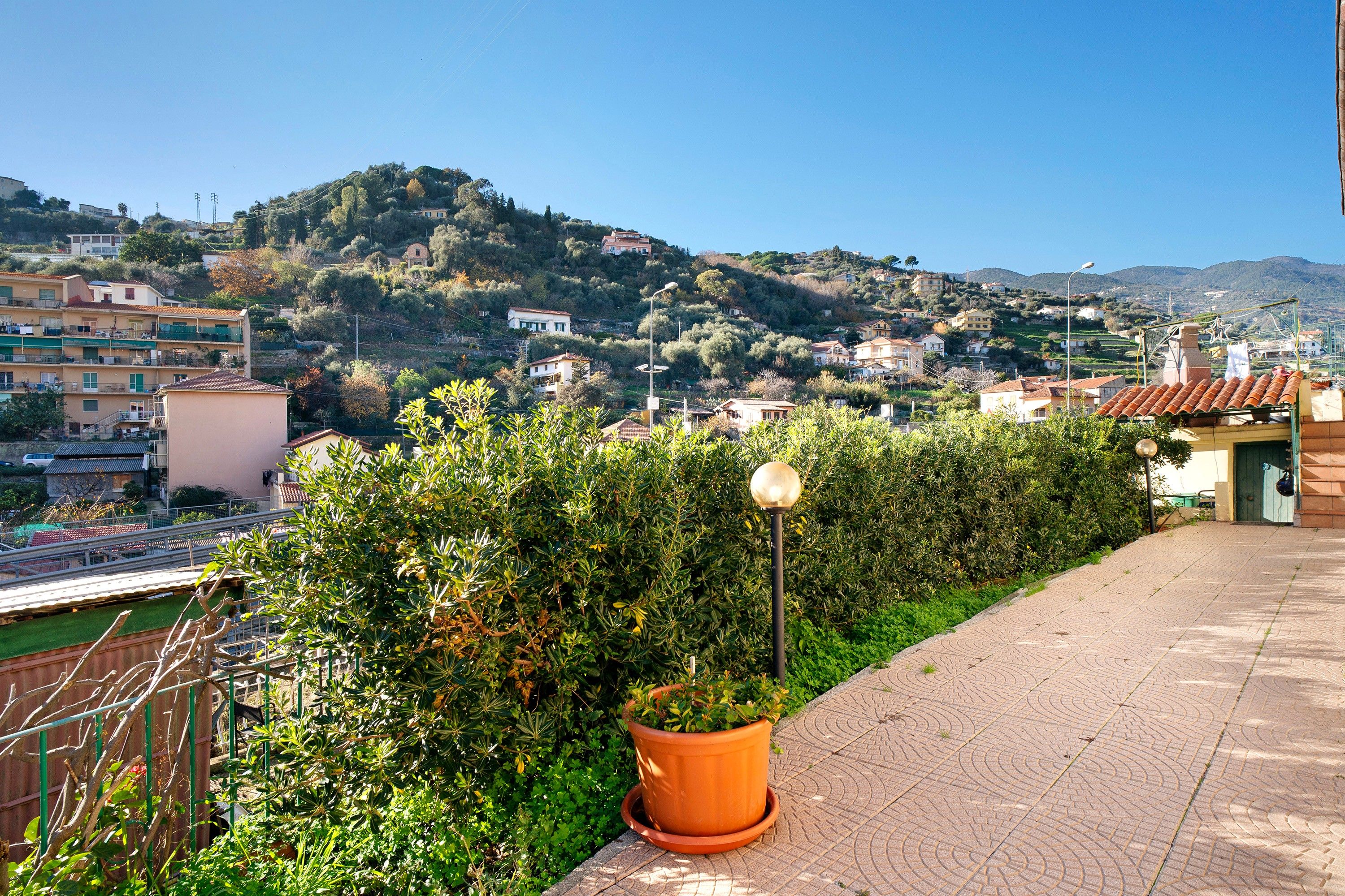 Un quartier résidentiel offrant une vue sur une colline, avec un chemin piétonnier pavé et un pot de fleurs.