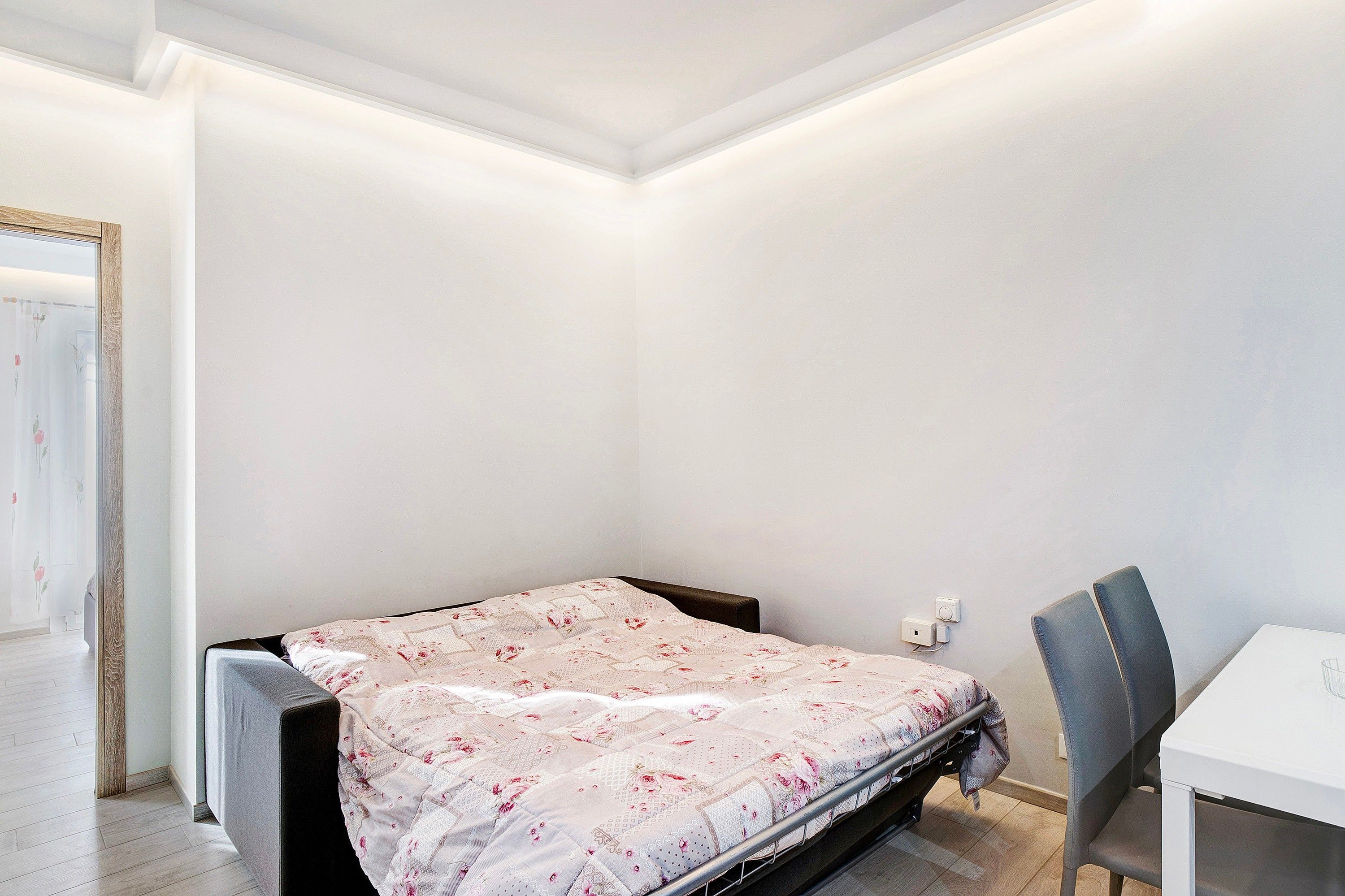 A small, neatly arranged bedroom with a single bed, a chair, and a table.