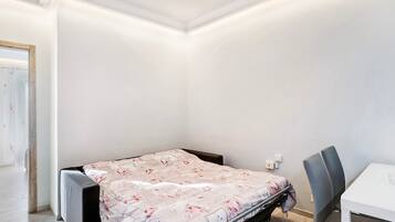 A small, neatly arranged bedroom with a single bed, a chair, and a table.