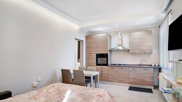 Un espace de vie compact comprenant un coin repas, une kitchenette et un lit recouvert d’une couvre-lit à motifs floraux.