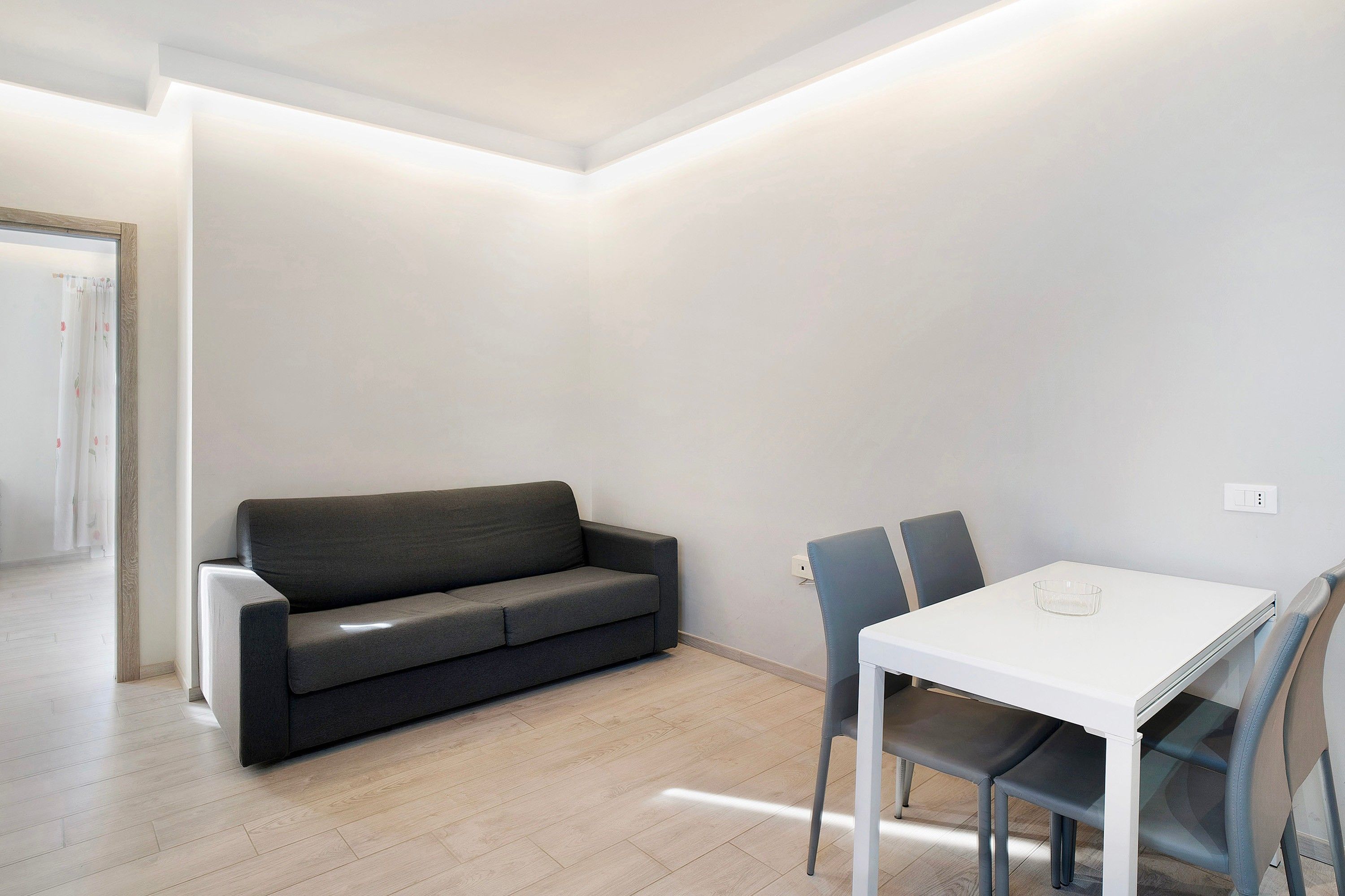 A modern, minimalistic room with a grey sofa, a white table, and two chairs.