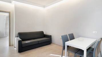 A modern, minimalistic room with a grey sofa, a white table, and two chairs.