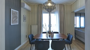 A dining area with a wooden table, six chairs, a chandelier, and a window with curtains. - Urban Luxury in the Heart of Athens (Athens)