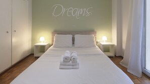A bedroom with a bed, two bedside lamps, a wall with the word "Dreams" written on it, and a window with curtains. - Cozy Athenian 1br: Pistachio Charm (Athens)
