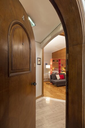 Una puerta de madera que da a una sala de estar con un sofá, una estantería roja y una lámpara de pie.