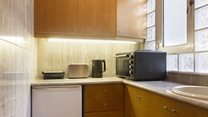 Uma cozinha compacta com armários de madeira, micro-ondas, torradeira e uma tigela de limões sobre uma mesa vermelha.