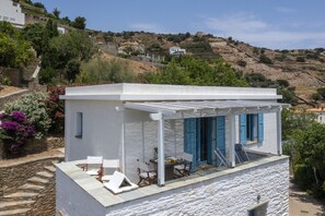 A white building with a covered patio, stone steps, and a view of a hillside with houses.