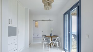 Un dormitorio moderno con cama, armario, zona de comedor con sillas y una mesa, y vista a través de una puerta.