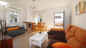 Ein Wohnzimmer mit einer Couch, einem Couchtisch, einem Esstisch mit Stühlen und Blick ins Freie.