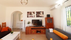 Ein modernes Wohnzimmer mit einer Couch, einem Fernseher auf einer Holzkommode und einem Esstisch mit einer Pflanze.