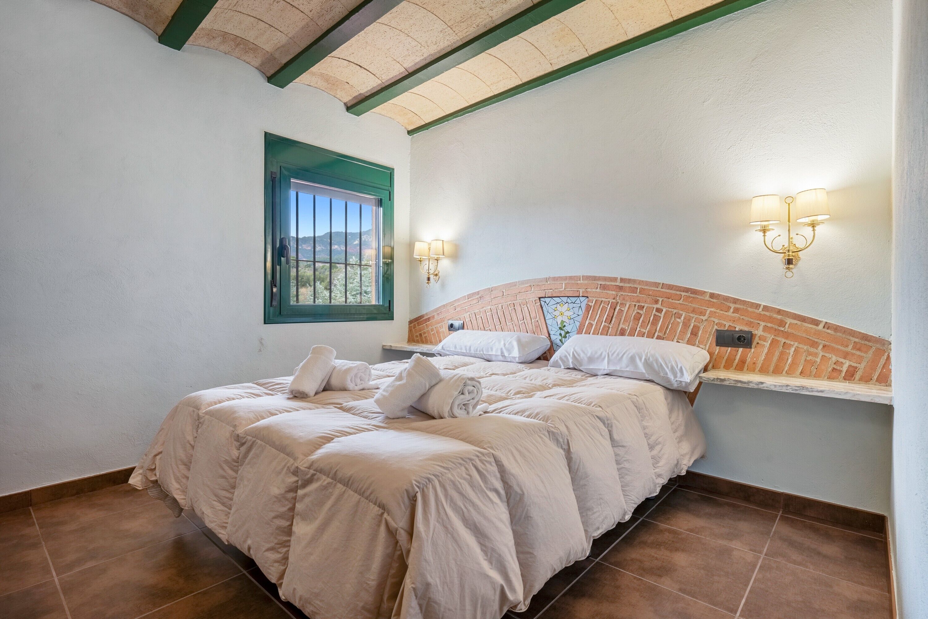 A bedroom with a brick headboard, a window with a green frame, and two wall-mounted light fixtures.