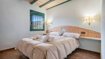 A bedroom with a brick headboard, a window with a green frame, and two wall-mounted light fixtures.