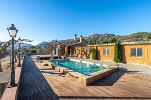 Un espace piscine doté d’une terrasse en bois, d’une piscine et d’un bâtiment avec un toit recouvert de tuiles.