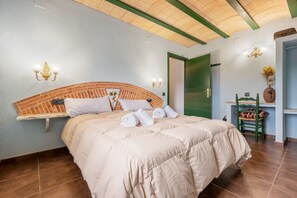 A bedroom with a brick headboard, a bed with a beige duvet, two wall sconces, a green door, and a small table with a vase. - Vacation Home "Mas Lucena" with Private Pool, Private Terrace & Wi-Fi (Alforja)