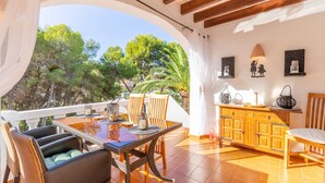 A dining area with a table and chairs, a wooden cabinet, and a view of trees through an archway. - Apartment 'Sillero Dos' with Shared Pool, Private Terrace and Air Conditioning (Moraira)
